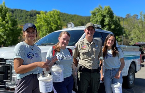 4 people standing in front of a truck, holding buckets of native wildflower seeds