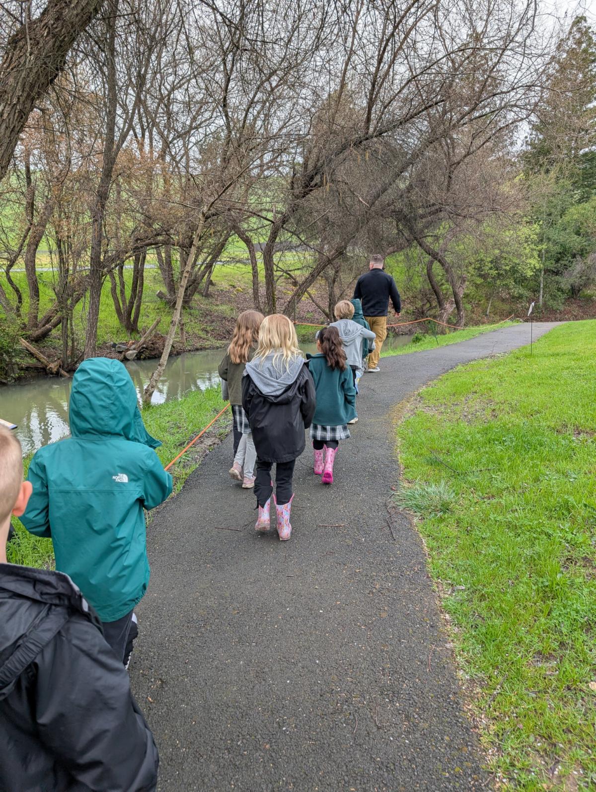 a group of children follow a tour guide near a stream