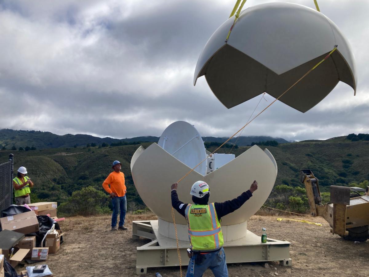 workers in safety vests and hard hats guide the installation of a large dome shaped structure