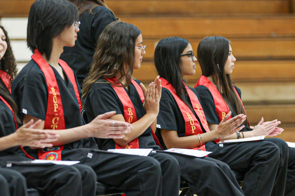 four students wearing red sashes applauding from their seats