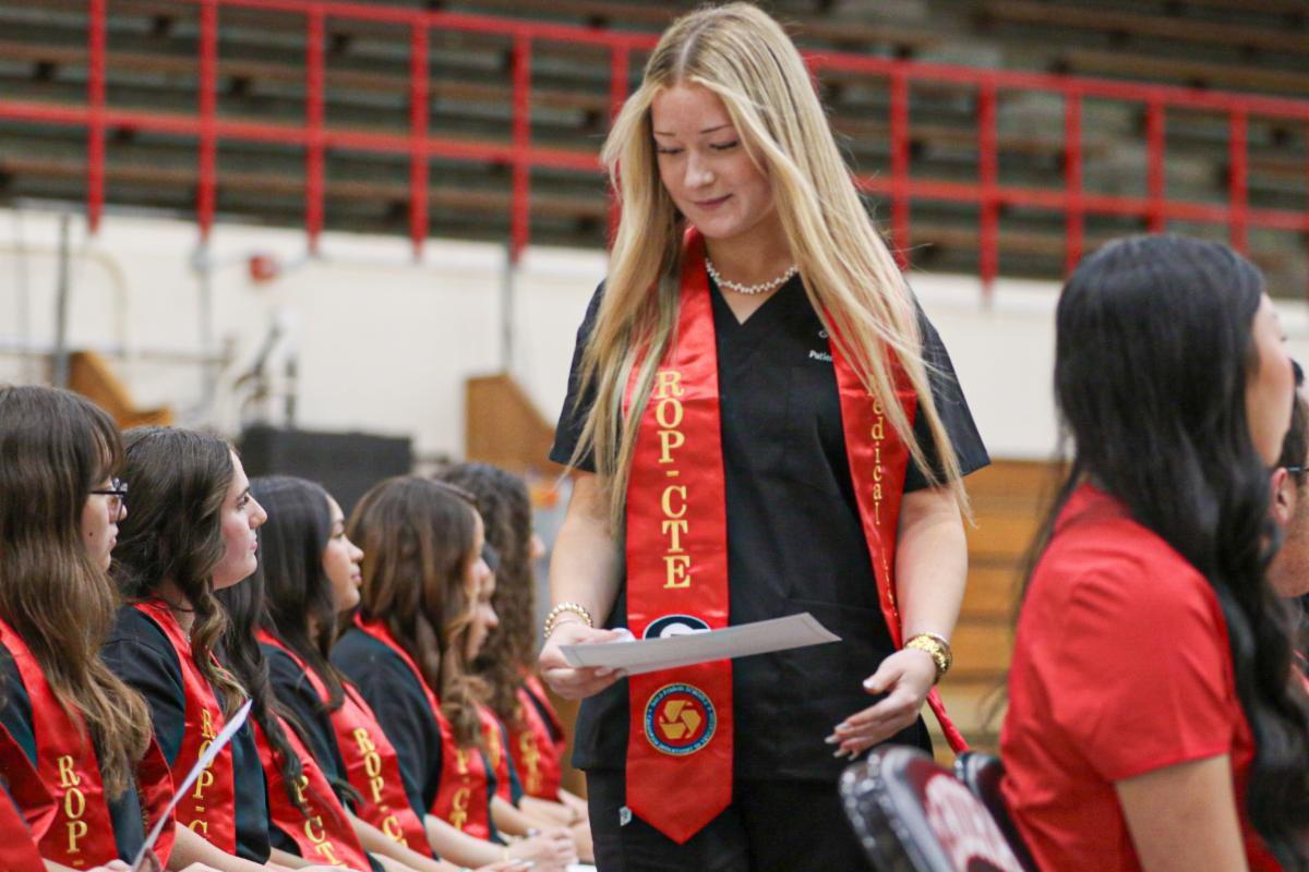 Student wearing a red sash and black scrubs walking back to her seat while carrying her certificate