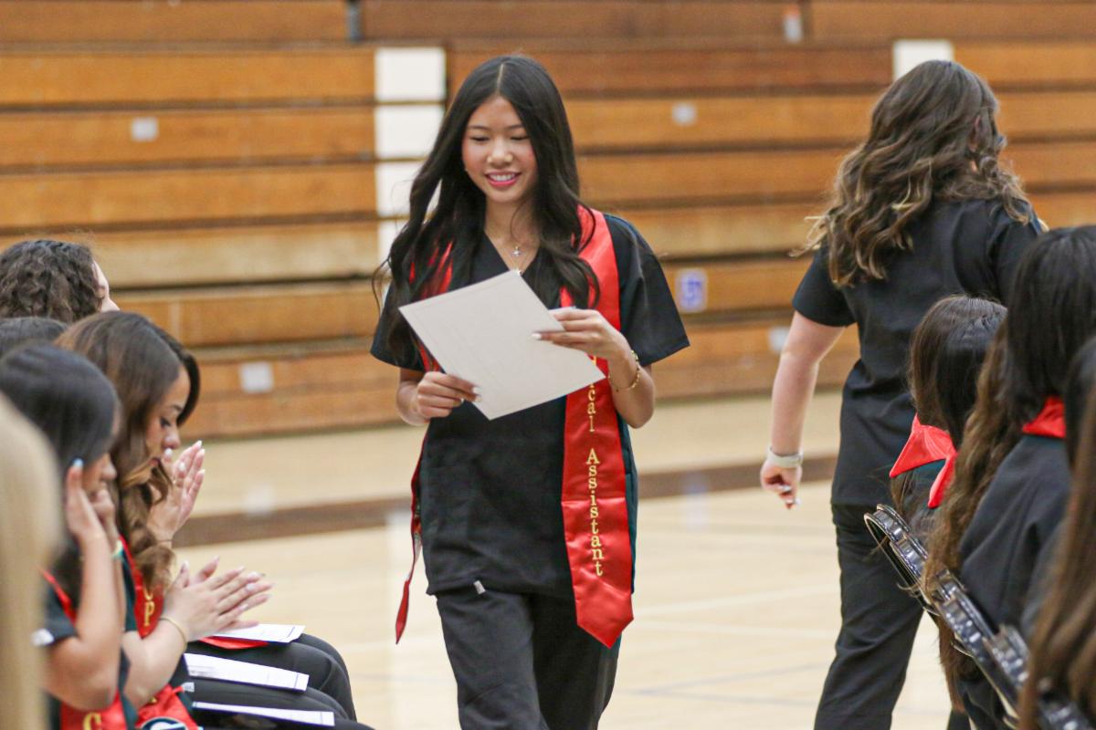 Student wearing a red sash walking back to her seat while smiling