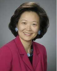 Theresa Chang smiles at the camera while wearing a dark pink suit jacket. Her dark, feathered hair is above her shoulders.