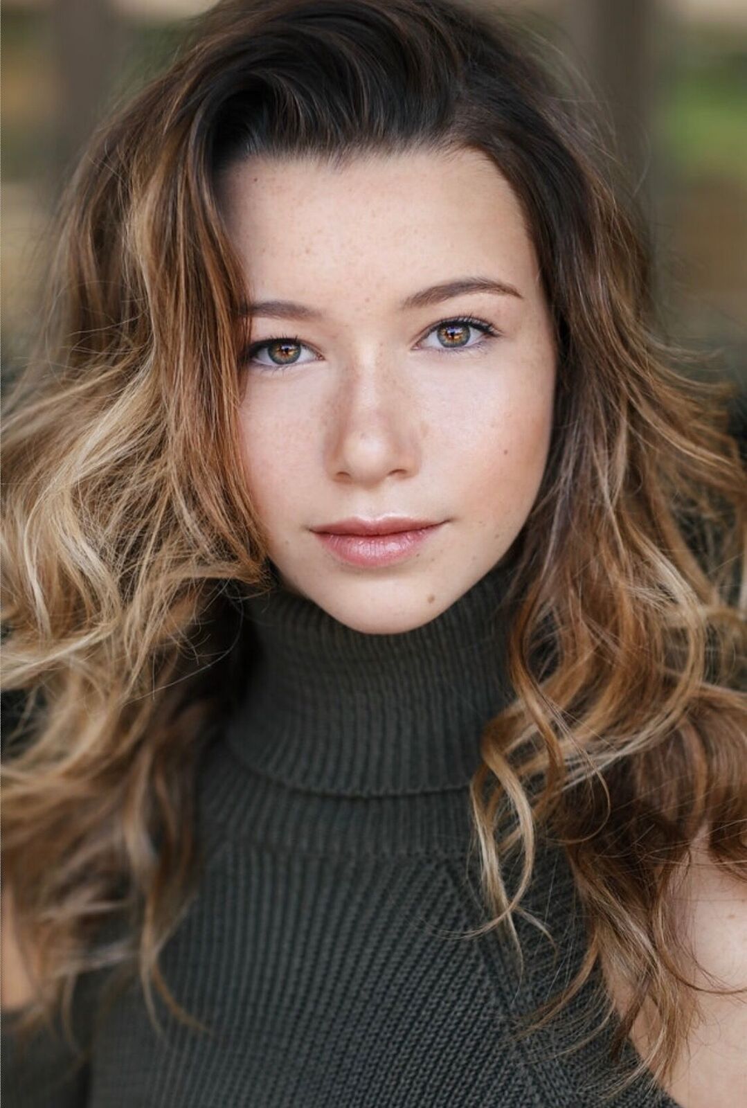 In a 2018 headshot Ava Noble looks at the camera as her blonde hair swirls around her. She wears a black sleeveless turtleneck.