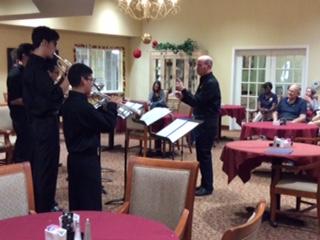 A group of musicians play brass instruments for senior citizens.