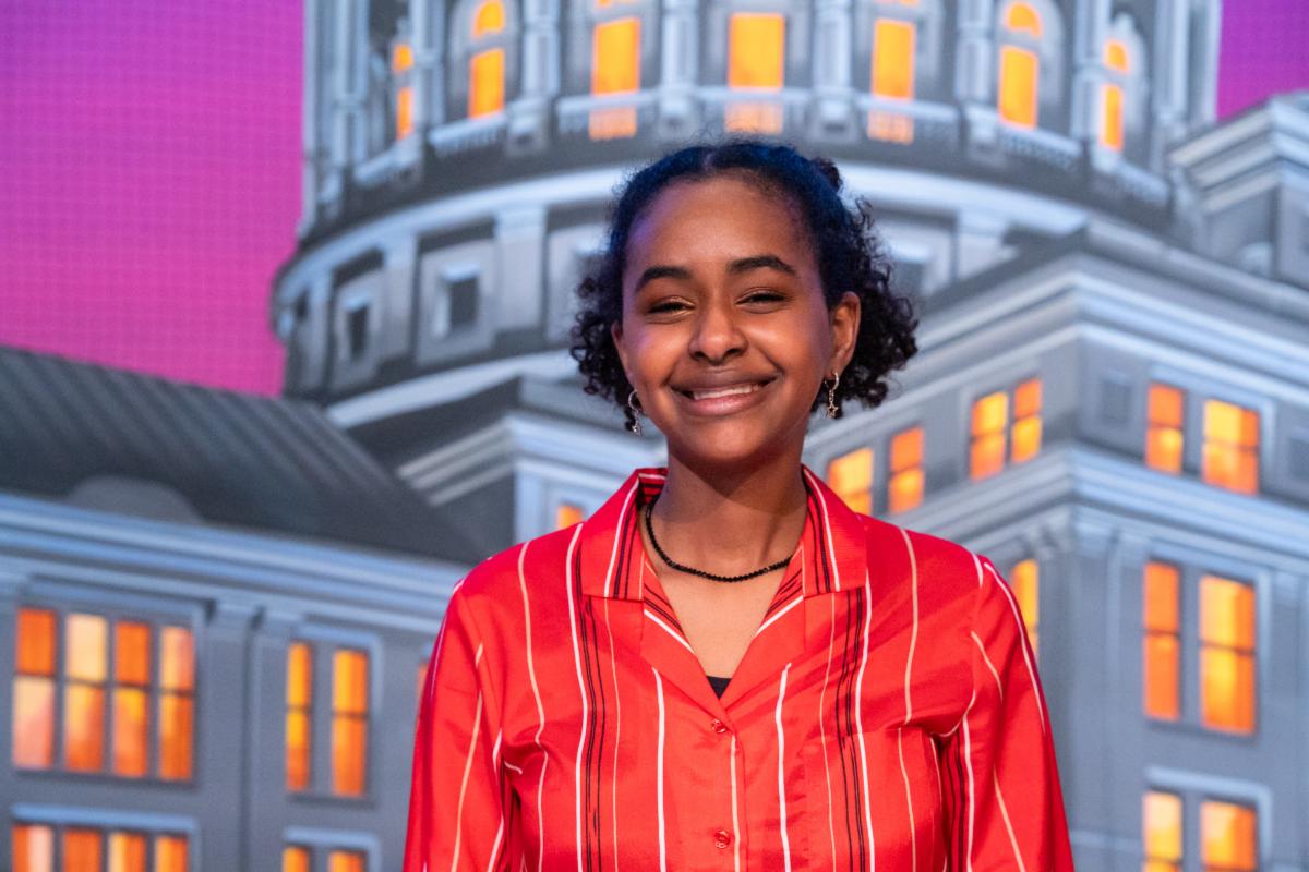Almaz Clawson smiles and stands in front of a stylized projection of the Texas Capitol