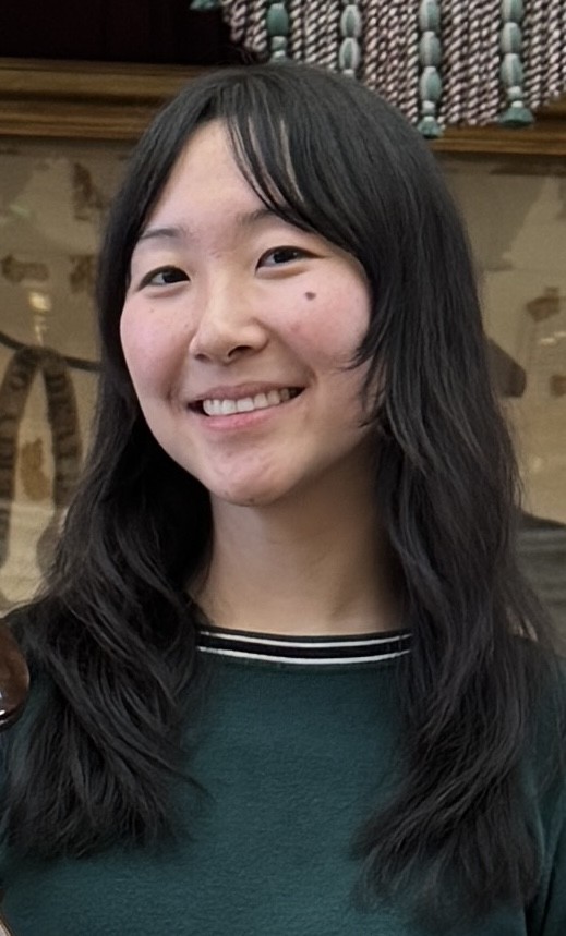 Doreen Shi smiles warmly at the camera. Her dark wavy hair falls past her shoulders. She wears a dark shirt.