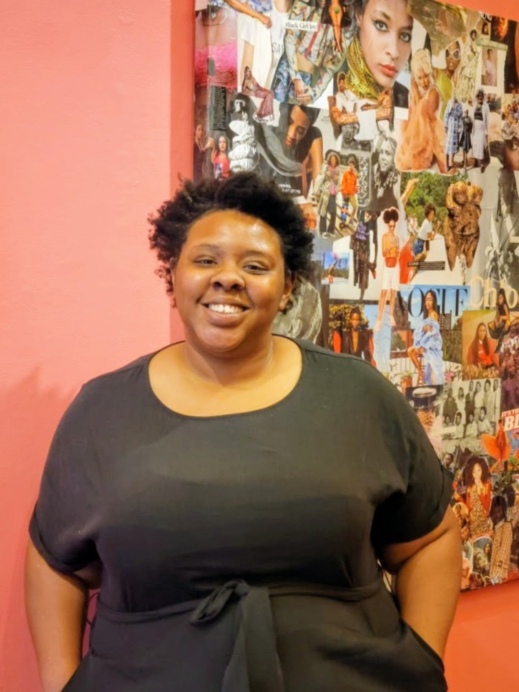 Danielle Demetria East stands with her had on her hip and her head at a slight angle toward the same side. She smile broadly at the camera.