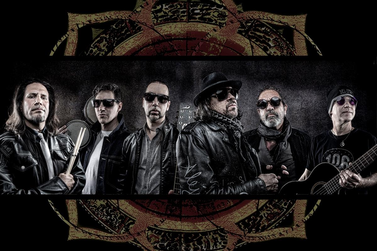 The six members Del Castillo, dressed in dark clothing and sunglasses, stand alongside each other and face the camera.
