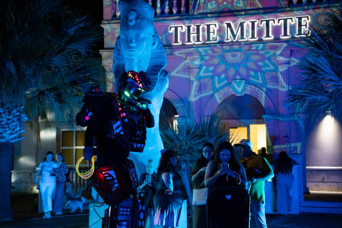A neon-highlighted performer is shown outside at night in the Mitte Cultural District.