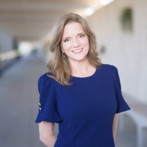 Alecia Lawyer tilts her head slightly and smiles at the camera. She has light red hair and wears a blue shirt.