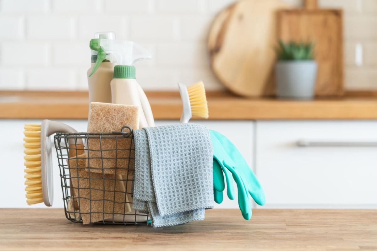 Wire basket full of various home cleaning supplies sitting on a wooden counter