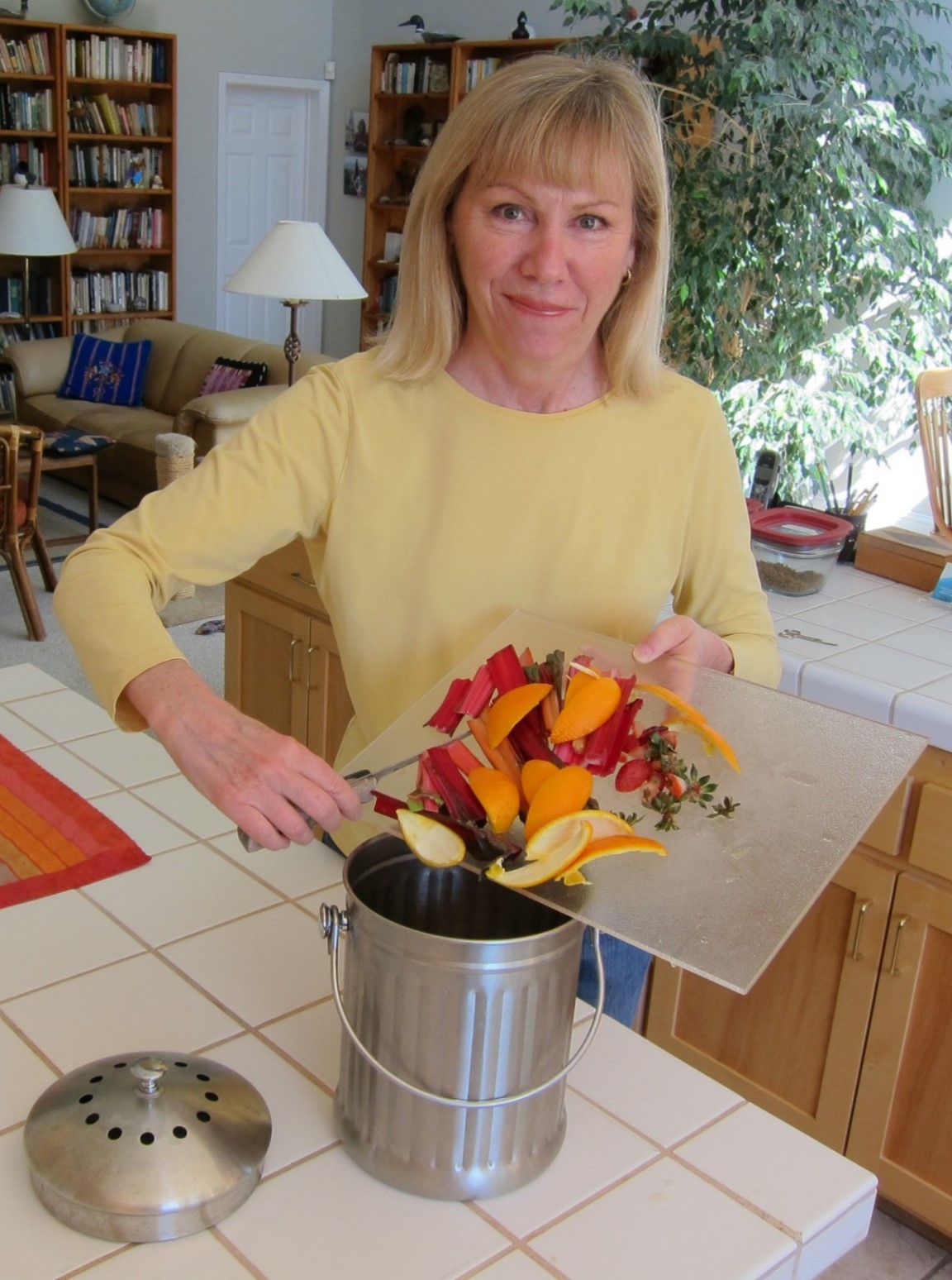 Woman smiling as she disposes of food scraps into a countertop compost bin
