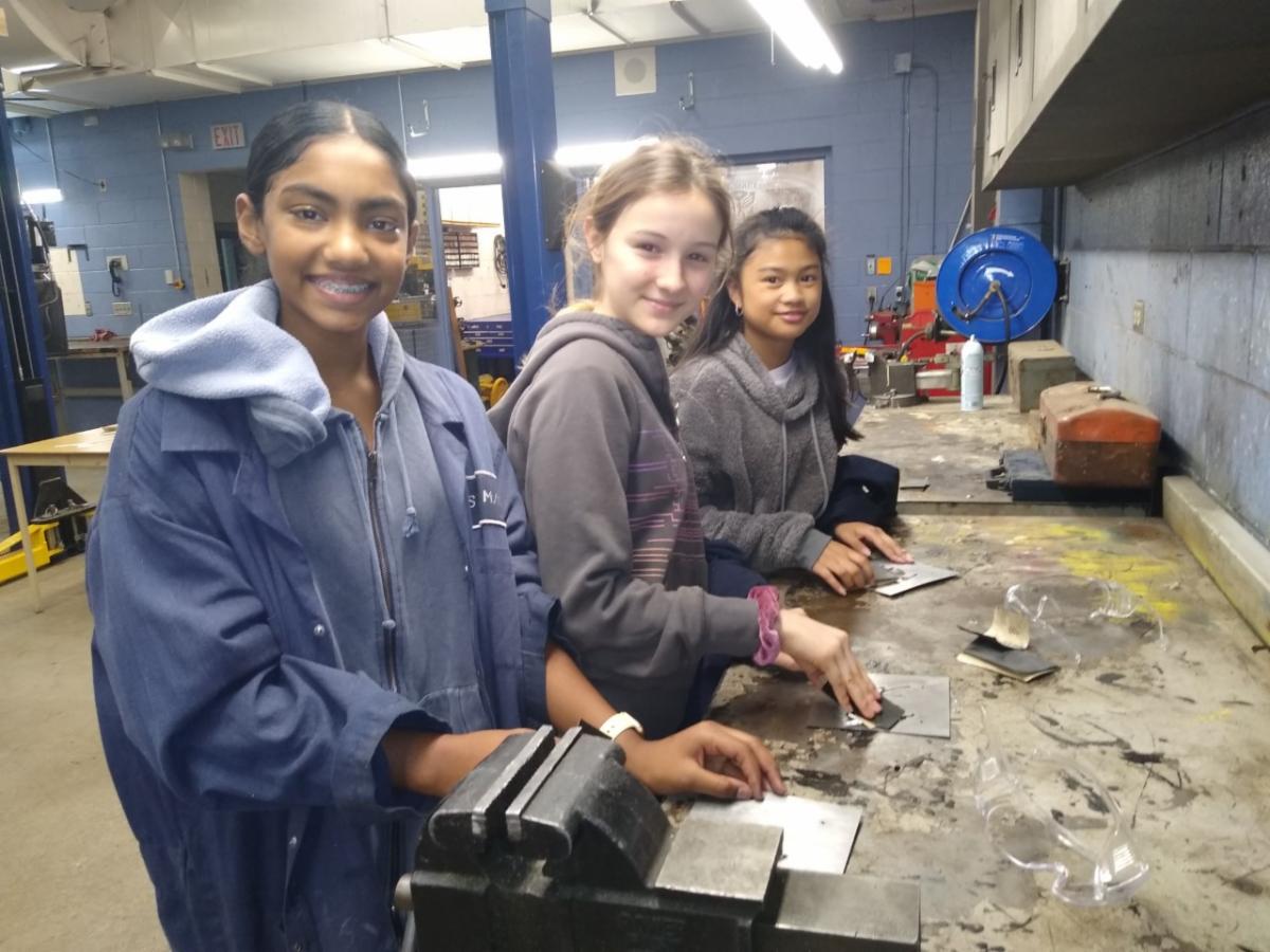 Three female students in a tech shop building a sign.