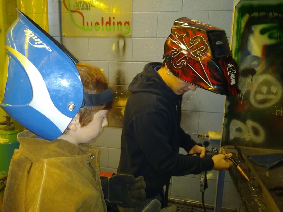 Male elementary student learns how to start a welding machine in a school's tech shop.