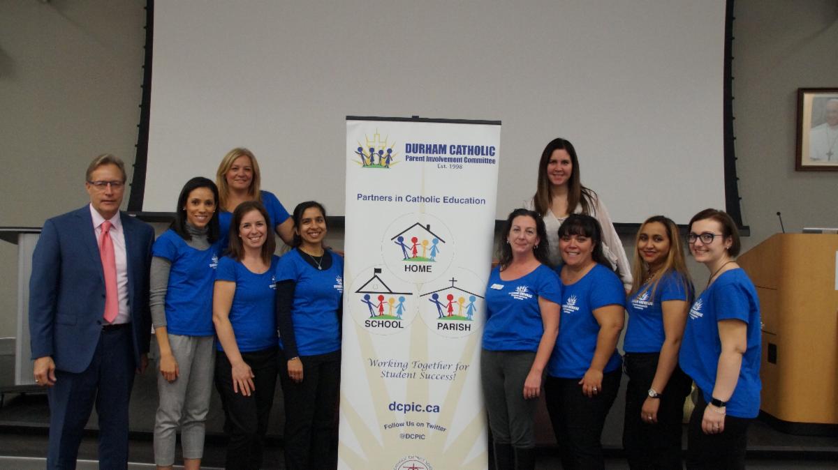 Members of the Durham Catholic Parent Involvement Committee standing by the committee's promotional pop-up banner.