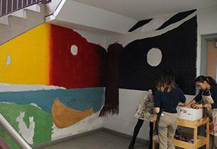 Three female student painting an Indigenous mural in the hallway of a secondary school.