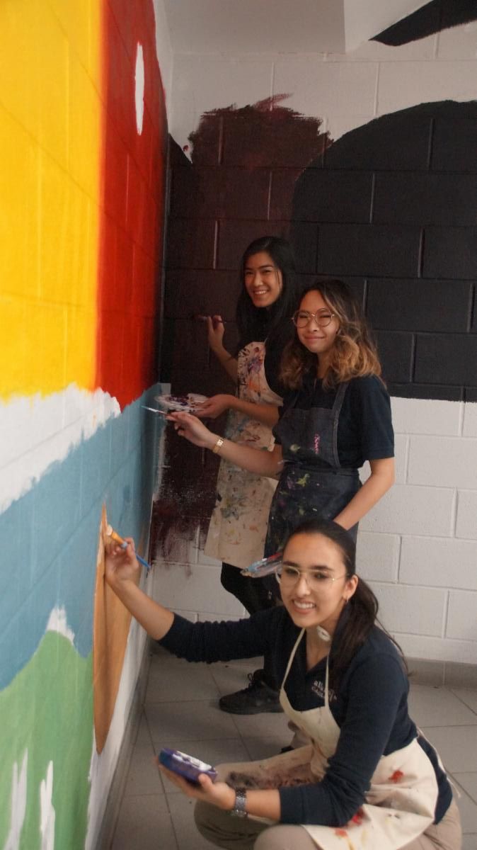 Three female students painting the Indigenous Education mural on the walls in a school's stairwell.