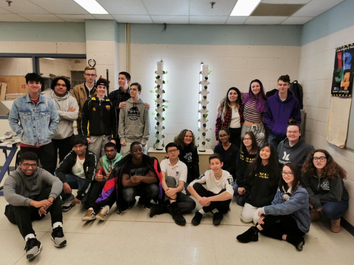 A group of male and female Green Industries students standing and sitting around the aeroponic gardening system.