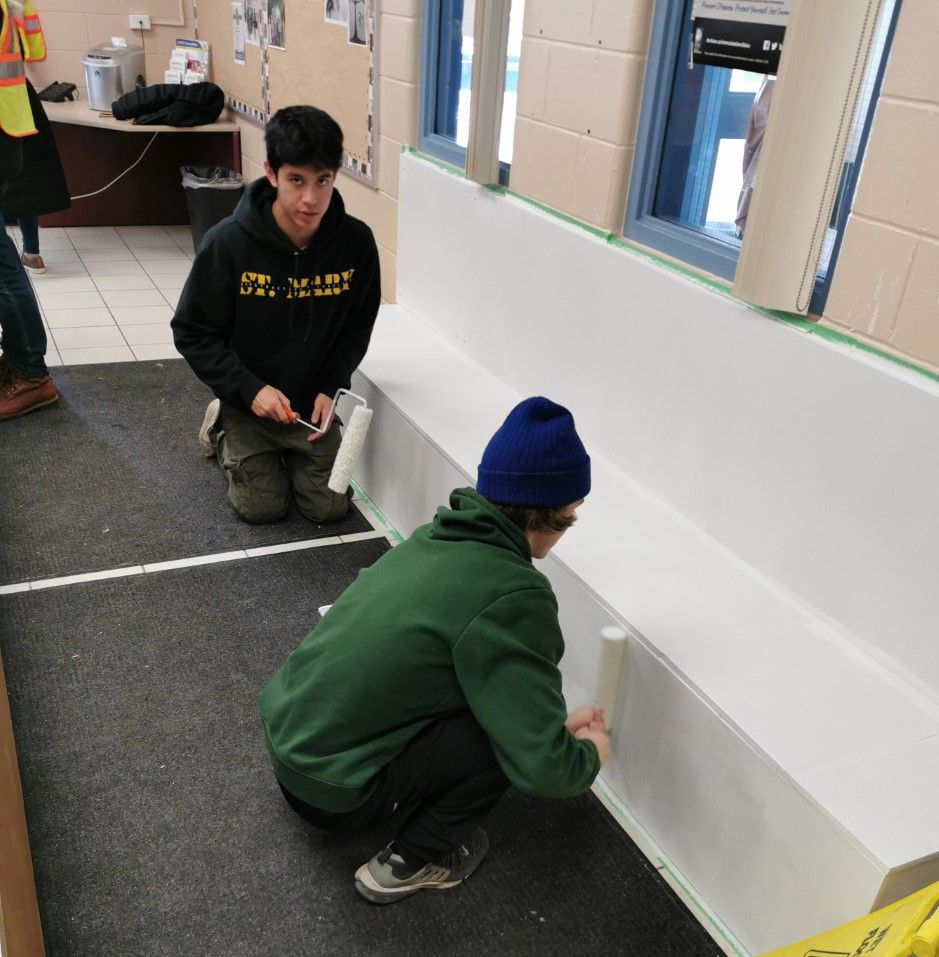 Two male students painting the bench white.