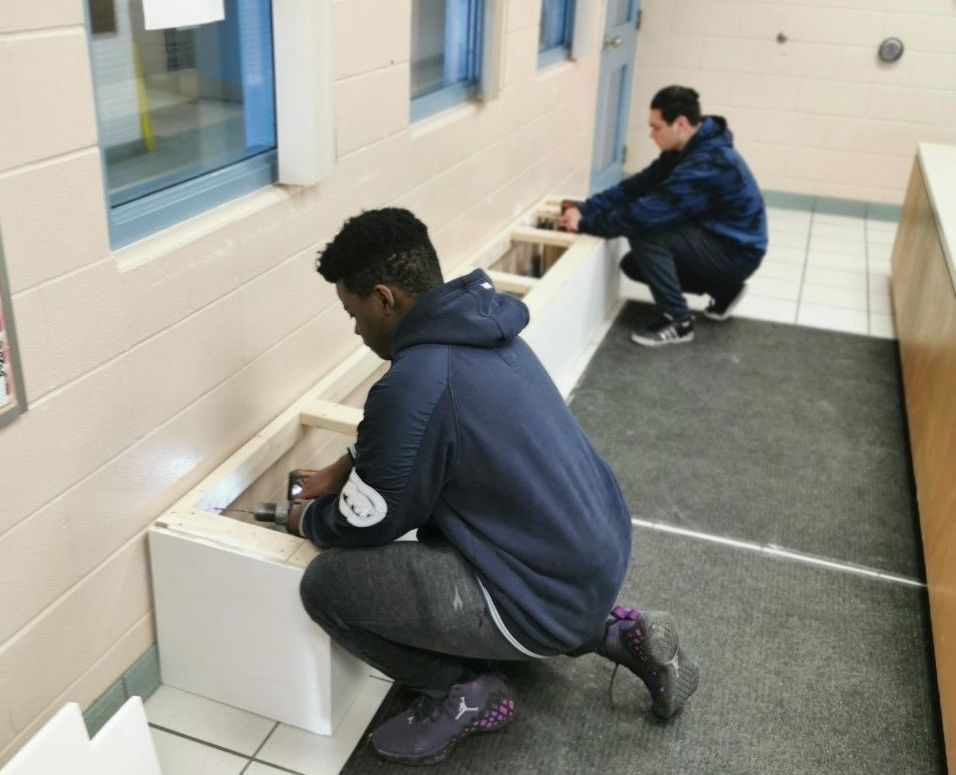Two male students installing the bench in school office.