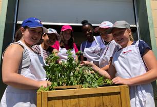Six female students picking herbs and wearing aprons and hats