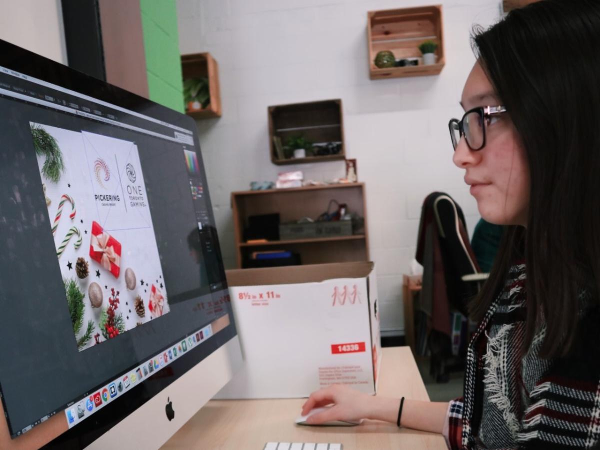 Female student working on a MAC computer designing an invitation.