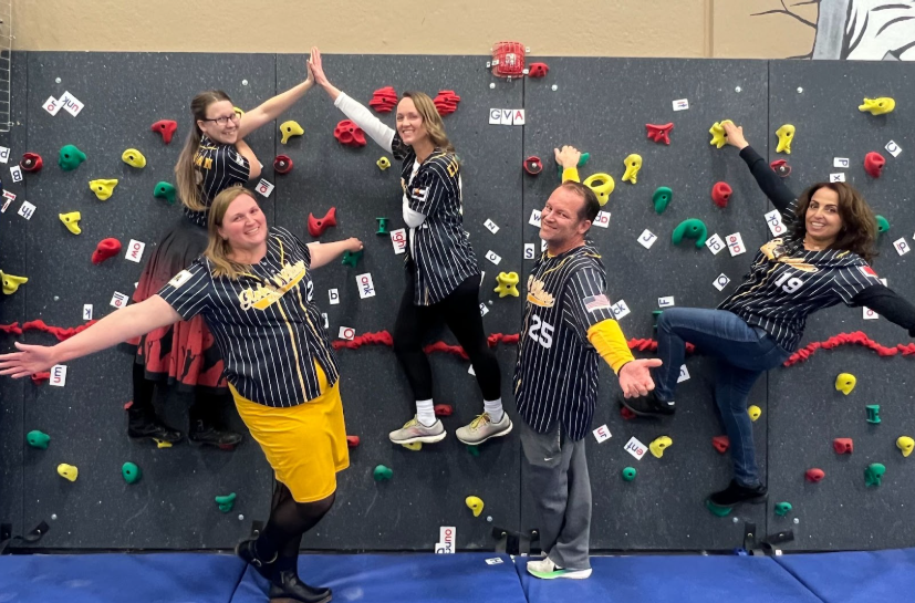 GVA Aurora Specials Team Members posing with outstretched arms in front of the school's rock climbing wall