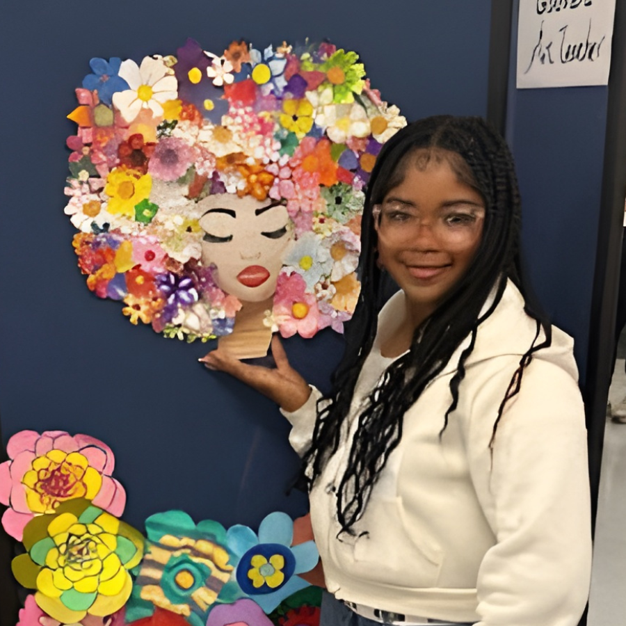 A student lifting her hand up to a piece of art she created