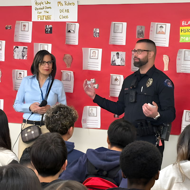 two adult presenters standing in front of a red wall filled with art