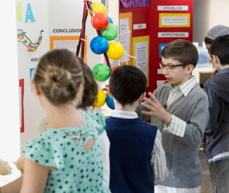 Four kids at a science fair explaining their projects to each other