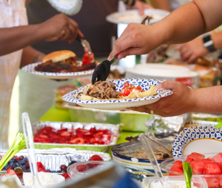 A tablescape of foods with hands scooping items onto their plates