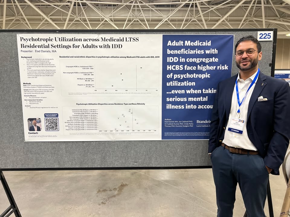 Elad Daniels stands beside his poster presentation on 'Psychotropic Utilization across Medicaid LTSS Residential Settings for Adults with IDD'.