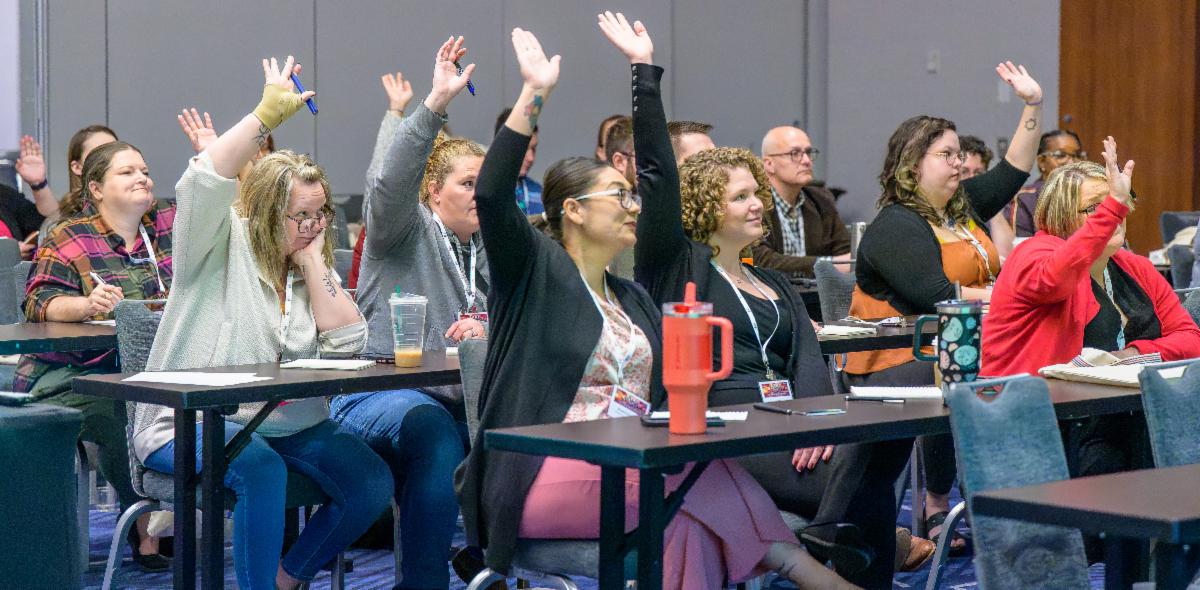 Group of people at a table raising their hands.