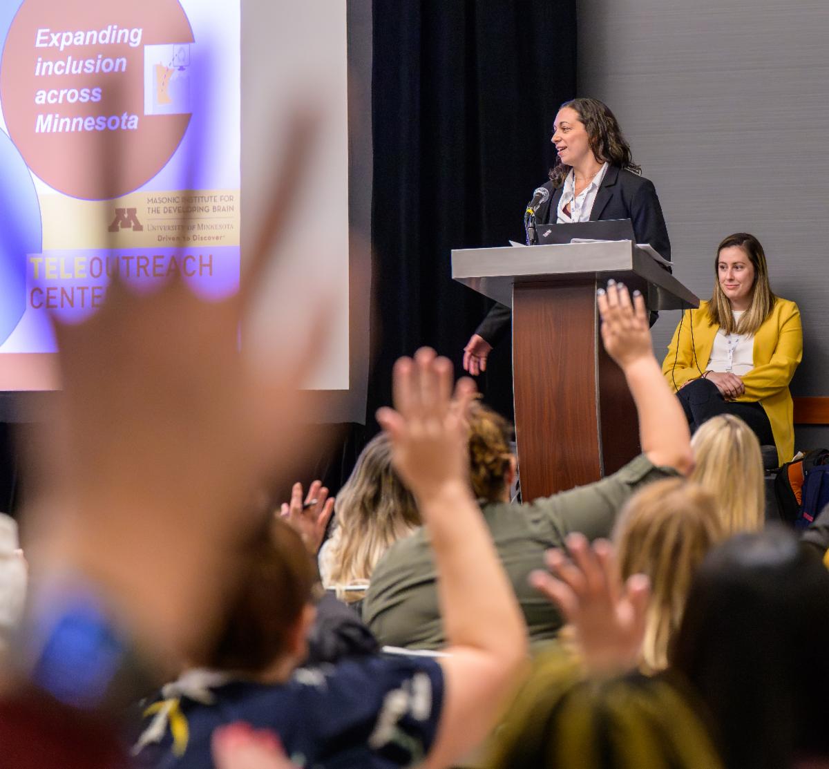 People raising their hands as a presenter speaks.