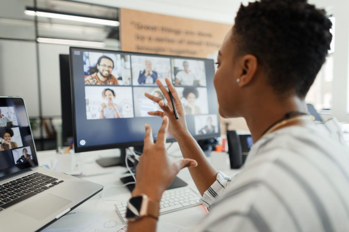 Woman participating in a virtual meeting from her computer, gesturing toward a screen displaying several video call participants.