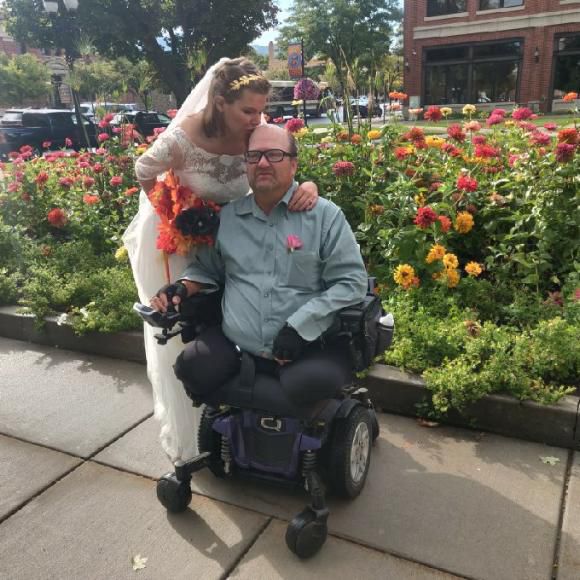 Sara and John at their wedding in front of bed of flowers.
