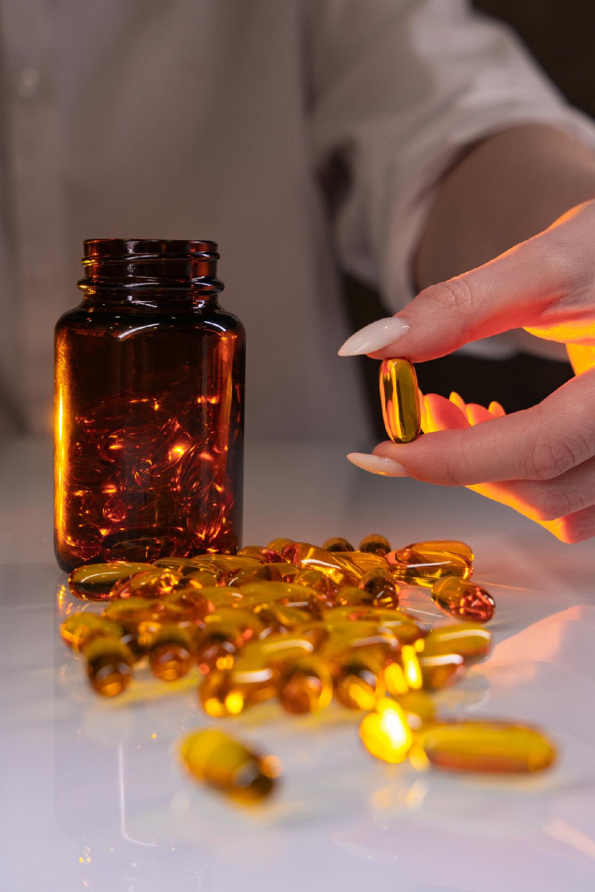 Close up of woman hand taking golden soft gel capsule from bottle. Healthcare vitamins supplements and wellness concept.