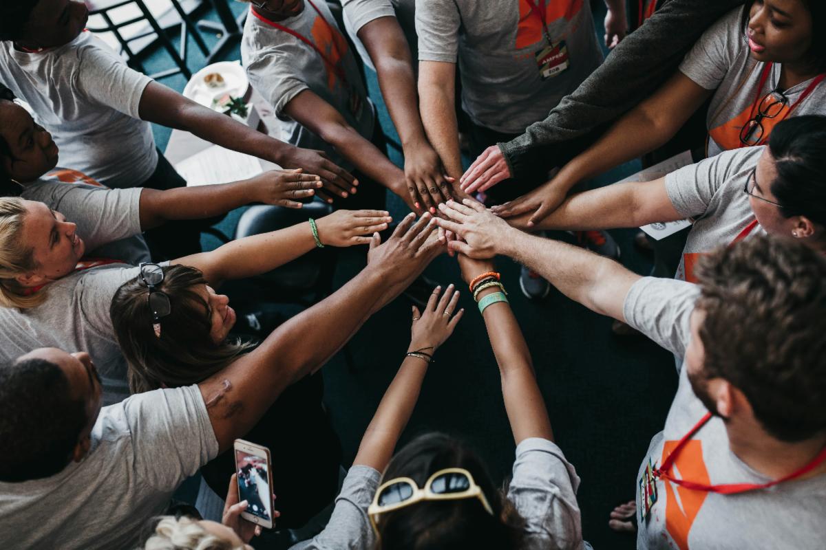 15 people have their arms in the middle in a team huddle