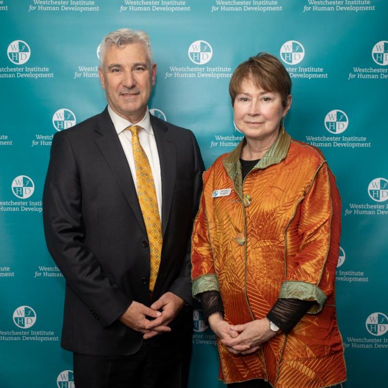 WIHD Board Chair Vera Halpenny and SVP of NYP Westchester Paul Dunphey in front of a WIHD branded step and repeat at the WIHD Spring Gala in May 2023.