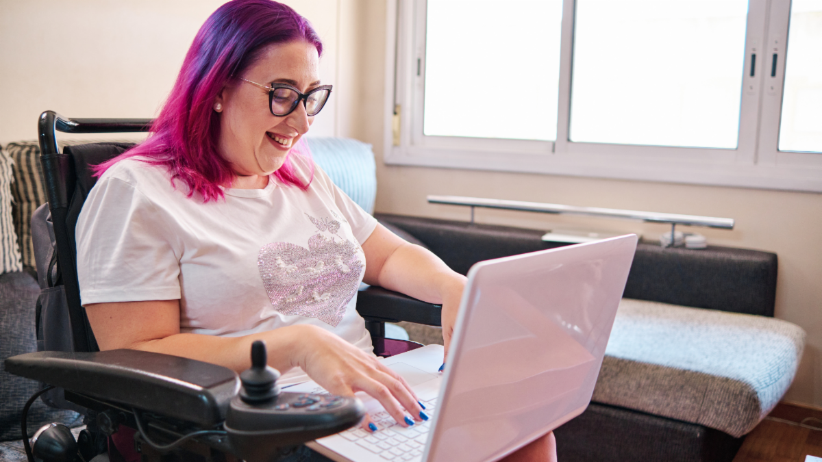 Woman using a laptop while seated in a power wheelchair at home.  