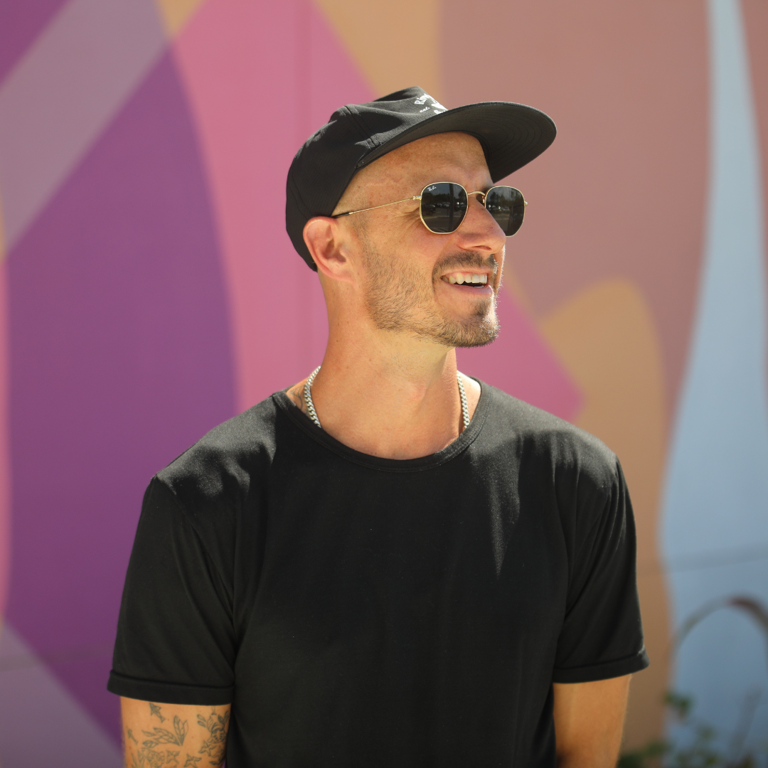 Artist Ben Heller smiles in front of his mural "Piece by Piece".