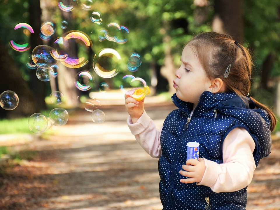 Little girl in blue vest blowing bubbles