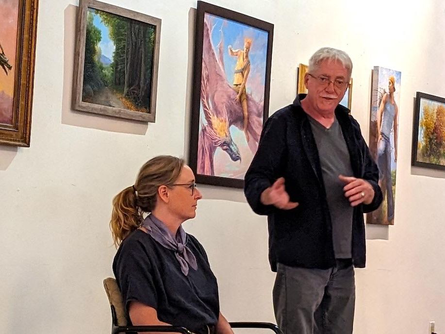 Alison Fox and Michael Erp standing in front of art pieces by Ray Passer as they present to the Rainbow Lounge group.