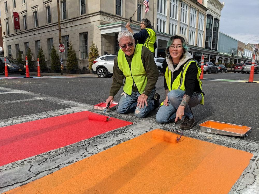 Michael and Beverly from the Center work together painting the red and orange stripes on the crosswalk pride painting.