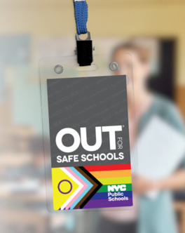 Photograph of an “OUT for Safe Schools” badge hanging from a blue lanyard, with blurred school staff member in background.