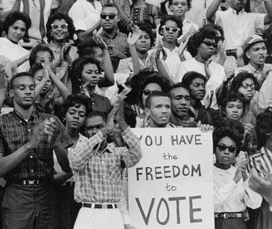 Black and white photo of civil rights advocates standing together with signs "You Have the Freedom to Vote"