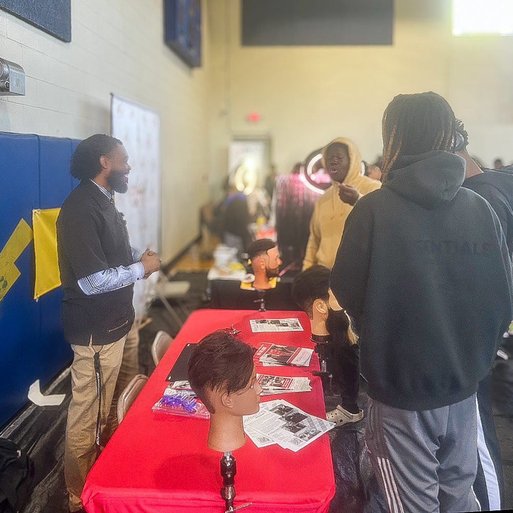 Barbering student speaks with high school students at booth.