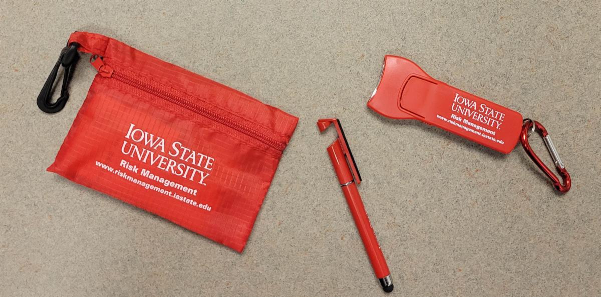 A small first aid pouch pen stylus and flashlight with carabiner in cardinal red with white print of Iowa State University Risk Management wordmark