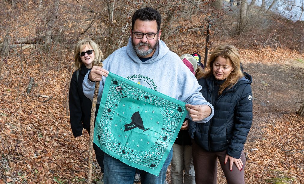 Three festival attendees with one holding up a bright green New York State bandana while hiking the Boulder's Loop.